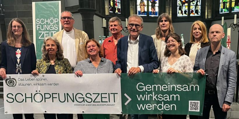 Personen hinter einem Banner der Aktion 'Schöpfungszeit'