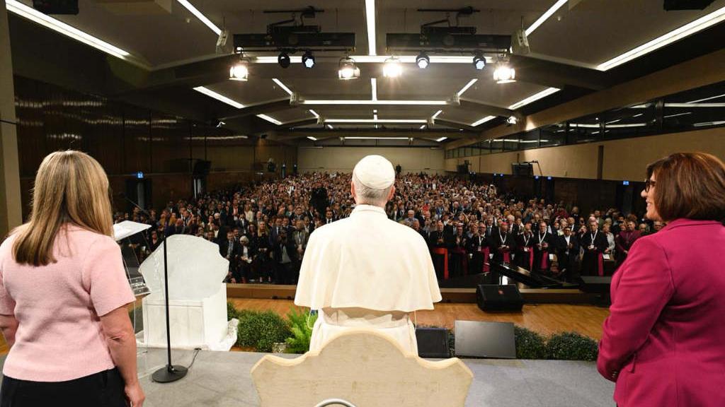 Papst Leo XIV. und zwei Frauen auf der Bühne vor einer mit Menschen gefüllten Halle