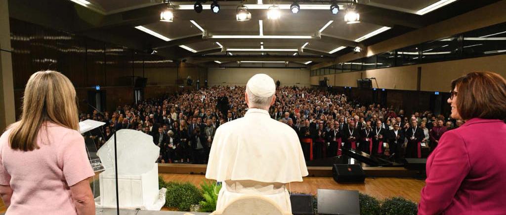 Papst Leo XIV. und zwei Frauen auf der Bühne vor einer mit Menschen gefüllten Halle