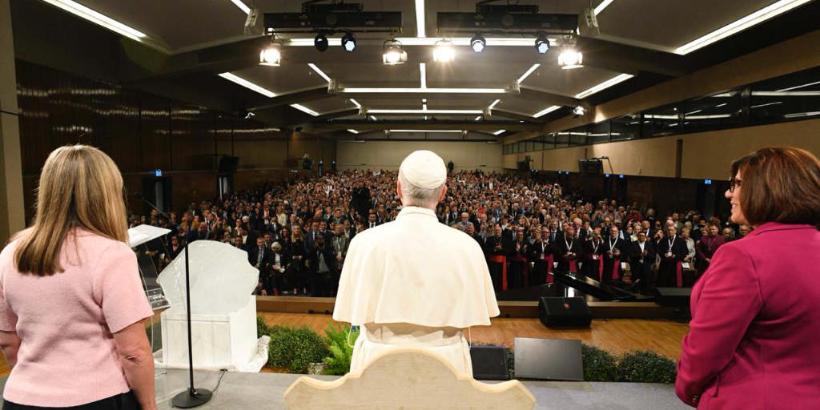 Papst Leo XIV. und zwei Frauen auf der Bühne vor einer mit Menschen gefüllten Halle