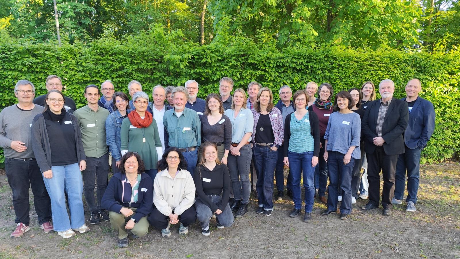 ca 30 Menschen vor einer grünen Hecke
