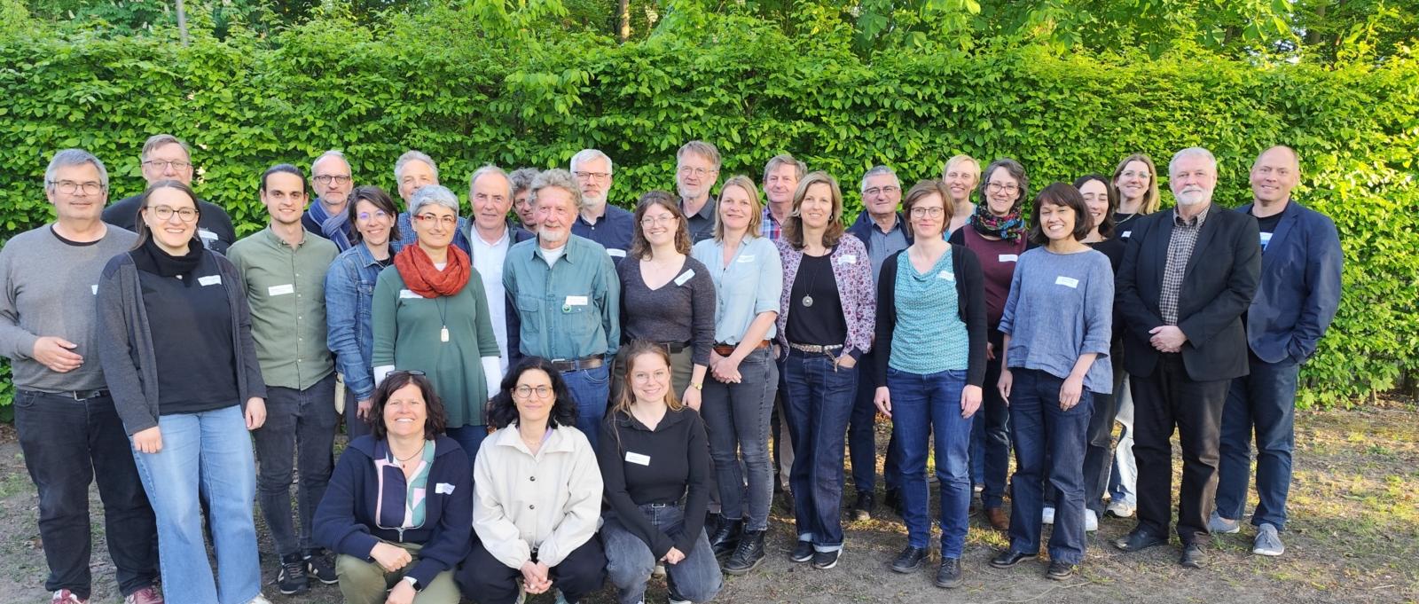 ca 30 Menschen vor einer grünen Hecke
