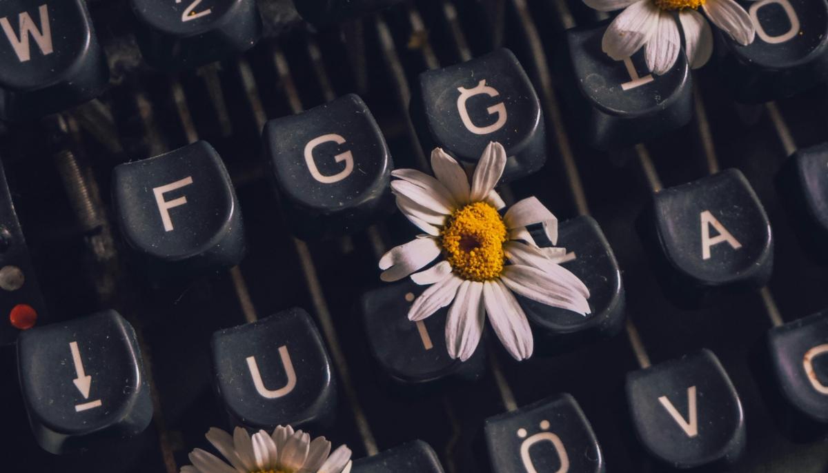 Die Tastatur einer Schreibmaschine mit drei Blumen zwischen den Tasten